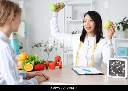Nutrizionista asiatica femminile che mostra il manichino e la mela al paziente in ufficio Foto Stock