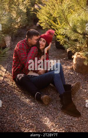 Ritratti ravvicinati di giovani coppie che si rilassano nella foresta, indossando camicie a scacchi rosse sedute tra le piantine dell'albero di Natale al mercato di strada. Man embra Foto Stock