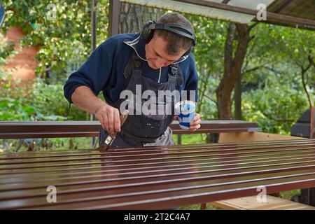 Un uomo in tuta da lavoro dipinge tubi metallici Foto Stock