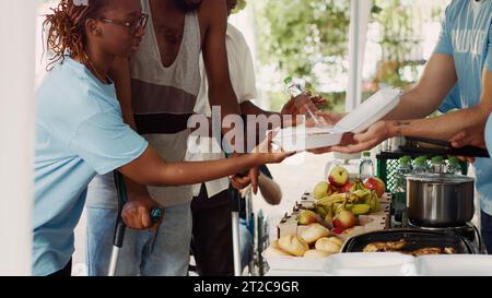 Le persone volontarie contribuiscono e offrono aiuto umanitario ai bisognosi e svantaggiati. La giovane volontaria nera aiuta un ragazzo afro-americano a usare stampelle durante un viaggio di cibo. Scatto con treppiede. Foto Stock