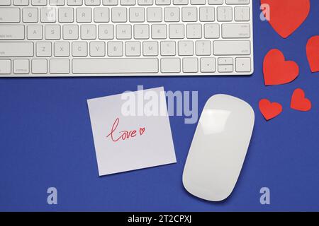 Concetto di relazione a distanza. Mouse per computer, tastiera, note d'amore e cuori di carta su sfondo blu, posizionamento piatto Foto Stock