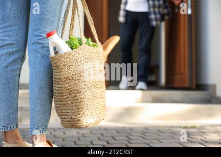 Aiutare i vicini. Donna con sacchetto di vimini con prodotti che visitano l'uomo all'aperto, primo piano Foto Stock