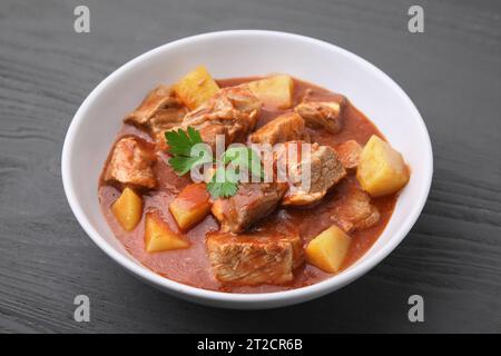 Delizioso gulasch in ciotola su un tavolo di legno nero, primo piano Foto Stock