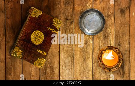 Un vecchio libro con copertina decorativa con candela su un vecchio tavolo da tavola Foto Stock