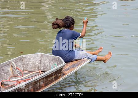 Una donna siede sulla prua di una barca e sta pagaiando con una pagaia, Thailandia Foto Stock