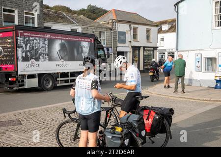 Uomo e donna con biciclette da turismo che indossano bavaglini Tour of Britain a Padstow, Cornovaglia, 2023 settembre, Inghilterra Foto Stock