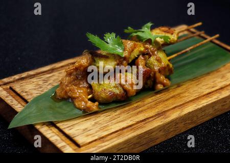 spiedino di satay di pollo indonesiano con salsa piccante di arachidi su una foglia di bambù con sfondo nero Foto Stock