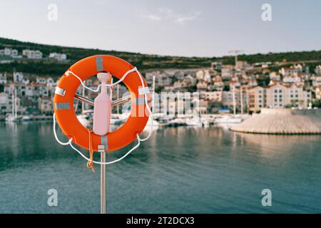 Lifebuoy su un palo d'acciaio con una chiusa in riva al mare sullo sfondo di case colorate sulla costa Foto Stock