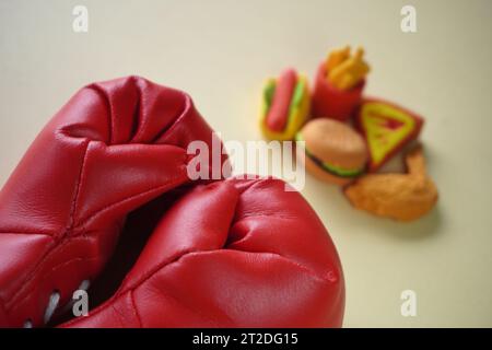 Immagine ravvicinata di guanto da boxe e cibi spazzatura come hamburger e patatine fritte. Combattere le cattive abitudini alimentari. Foto Stock