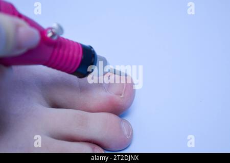 Il processo di fare una pedicure sulle punte della lavorazione del chiodo con l'aiuto di una macchina speciale su uno sfondo blu. Foto Stock