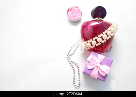 Una bella bottiglia di profumo femminile in vetro trasparente rosa decorata con perle bianche e una candela a forma di piccola confezione regalo blu rosa Foto Stock