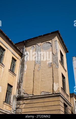 Facciata dell'edificio fatiscente. Intonaco esterno incrinato e sbucciato su pareti in mattoni e vecchie telai delle finestre, niente persone. Foto Stock