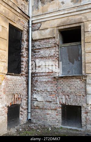 Facciata dell'edificio fatiscente. Intonaco esterno incrinato e sbucciato su pareti in mattoni e vecchie telai delle finestre, niente persone. Foto Stock