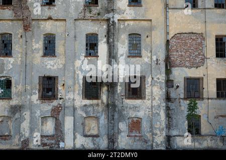 Facciata dell'edificio fatiscente. Intonaco esterno incrinato e sbucciato su pareti in mattoni e vecchie telai delle finestre, niente persone. Foto Stock