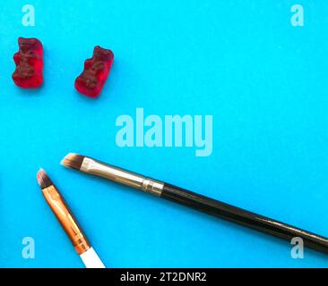 le spazzole per il trucco si trovano su uno sfondo blu opaco accanto agli orsi gommosi. due spazzole a setole fini si trovano accanto agli orsi gommosi rossi. dessert fatto a mano, torta d Foto Stock