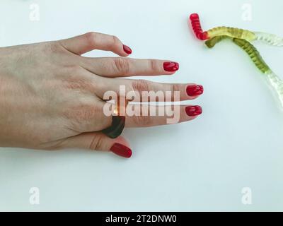 i vermi lunghi, appetitosi e multicolore giacciono sulla mano della ragazza con una manicure rossa brillante. il verme si intreccia sul dito della ragazza come un anello. th Foto Stock