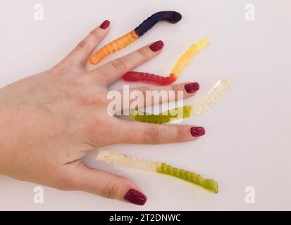 vermi lunghi, appetitosi e multicolori per mano di una ragazza con una manicure rossa brillante. i vermi giacciono tra le dita. riprese creative di br Foto Stock