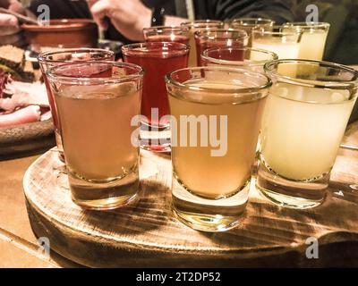 Un set di un sacco di deliziosi bicchieri gialli arancioni rossi, shot con alcol forte, vodka, ripieno, brandy su banchi di legno su un tavolo in un caffè, bar, re Foto Stock