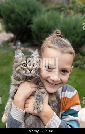 un ragazzo felice di 7-8 anni tiene con cura nelle mani vicino al viso un gatto amato dagli occhi grandi Foto Stock