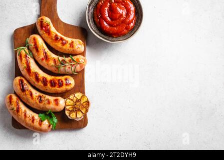 Salsicce grigliate con salsa di pomodoro ed erbe su sfondo bianco, vista dall'alto, spazio copia. Salsicce wurst arrostite fatte in casa su tavola di legno. Foto Stock