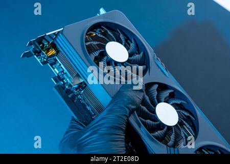 la mano di un tecnico informatico contiene una potente e moderna scheda per videogiochi per un computer con tre fan. Il concetto di hardware per PC. Video car di gioco Foto Stock