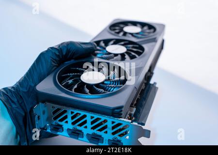 la mano di un tecnico informatico contiene una potente e moderna scheda per videogiochi per un computer con tre fan. Il concetto di hardware per PC. Video car di gioco Foto Stock