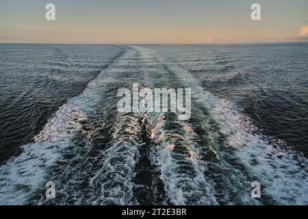 Nave da crociera con vista posteriore sul mare vuoto con tracce di onde e schiuma bianca creata dai motori della nave prima dell'alba. Concetto di viaggio e vacanza Foto Stock