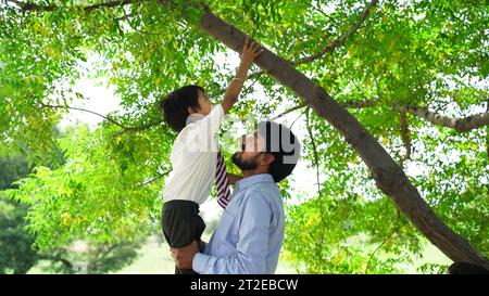 Ritratto di un figliolo sorridente e seduto sul collo del suo bellissimo padre isolato sullo sfondo della natura Foto Stock