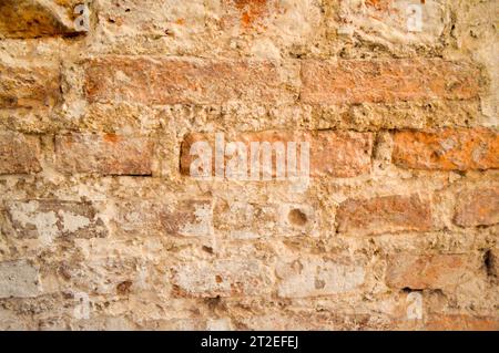 La consistenza dell'antico antico antico medioevale, robusto sbucciamento della parete graffiata di mattoni rettangolari rossi arancioni luminosi con cuciture e crepe. La Foto Stock