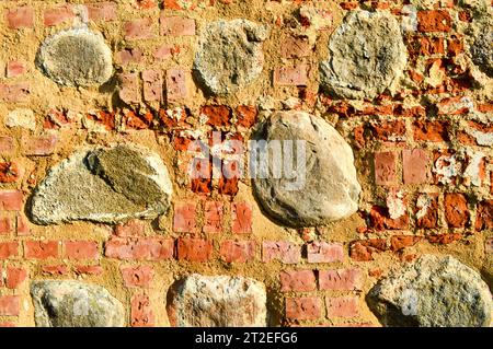 La consistenza dell'antica pietra medievale antica, il peeling duro, la parete di mattoni di argilla rossa rettangolare e grandi pietre, ciottoli. T Foto Stock