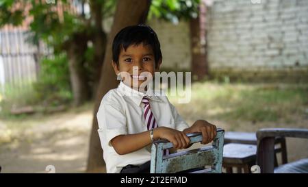 Ritratto di un allegro e allegro bambino di scuola indiana o di bambini in uniforme che alzano la mano in classe mentre studiano con libri e laptop. Apprendimento online Foto Stock