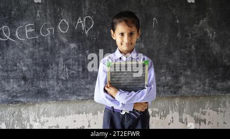 Una bambina di una studentessa indiana felice in piedi di fronte a una lavagna nera. Concetto di istruzione o ritorno a scuola Foto Stock