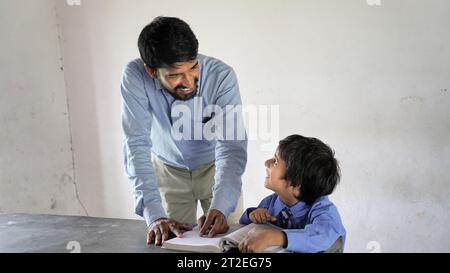 Insegnante indiano che insegna a uno studente di scuola rurale in classe, scena tipica in una scuola rurale o in un piccolo villaggio in India Foto Stock