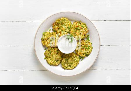 Frittelle di zucchine vegetariane vegetali su piatto su sfondo di legno bianco. Vista dall'alto, base piatta Foto Stock