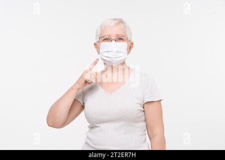 Ritratto di anziana donna caucasica che indossa la maschera medica in sfondo bianco isolato studio shot Foto Stock