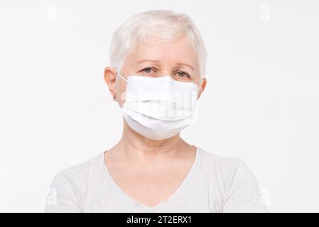 Ritratto alla testa di anziana donna caucasica che indossa la maschera medica in sfondo bianco isolato studio girato Foto Stock