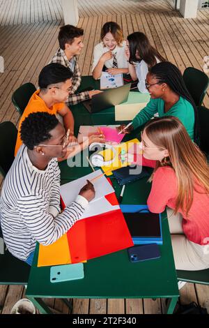 Vista verticale ad angolo alto di un grande gruppo di studenti adolescenti multirazziali che lavorano su un progetto di compiti universitari nella biblioteca delle scuole superiori. Lavoro di squadra di diversi giovani compagni di classe che studiano insieme. Foto di alta qualità Foto Stock