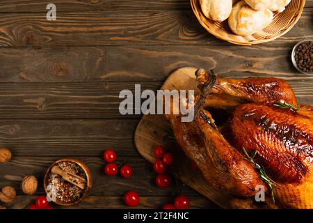 cena del giorno del ringraziamento, pane appena sfornato e pomodori ciliegini rossi vicino al tacchino arrosto su un tavolo di legno Foto Stock