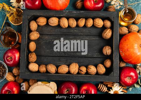 sfondo colorato per il giorno del ringraziamento con noci su vassoio di legno nero circondato da oggetti per il raccolto autunnale Foto Stock