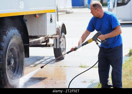 Autolavaggio per veicoli pesanti e cargo. Il lavavetri maschio in lava un camion con una pistola ad acqua in strada in un giorno d'estate. Foto Stock