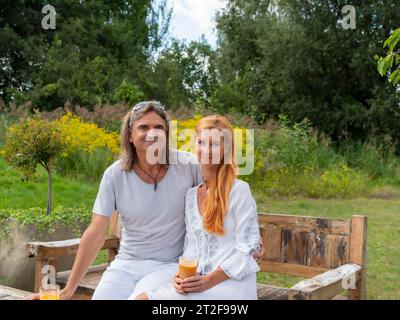 Uomo e donna in giardino su una panca da giardino, bevendo bicchieri con succo di frutta in mano, Germania Foto Stock