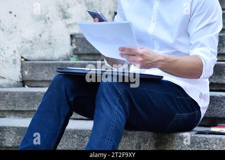 Uomo del commerciante seduto sulle scale e analizza i dati finanziari e i grafici sui documenti. Concetto di commercio e successo. Foto Stock