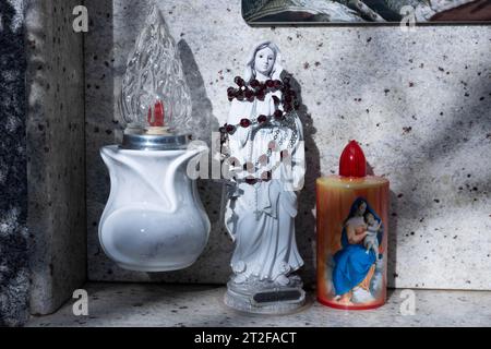Candele kitschy alimentate a batteria elettrica accanto a una piccola figura di Maria avvolta in rosario su una tomba a urna in un cimitero, Bari Sardo, Ogliastra Foto Stock