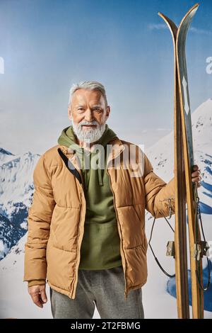 Uomo atletico vestito come Babbo Natale che tiene lo sci guardando la macchina fotografica con lo sfondo delle montagne, concetto invernale Foto Stock