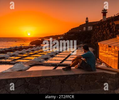 Un giovane seduto al tramonto del faro di Fuencaliente accanto alla miniera di sale, sulla rotta dei vulcani a sud dell'isola di Los Angeles Foto Stock