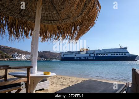 IOS, Grecia - 11 settembre 2023: Vista di un lettino, di un ombrellone e di un traghetto Blue Star che arriva al porto di iOS Grecia Foto Stock