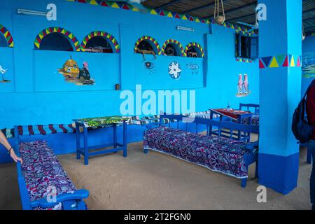 Una giovane donna con un vestito rosso che sale alcune scalinate colorate che salgono su una splendida terrazza di una tradizionale casa blu in un villaggio nubiano vicino Foto Stock