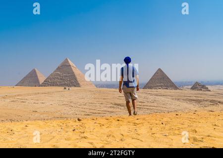 Un giovane in un turbante blu che cammina accanto alle piramidi di Giza, il monumento funerario più antico del mondo. Nella città del Cairo, in Egitto Foto Stock