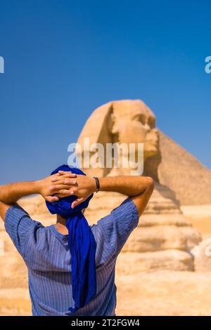 Un giovane turista che gode e ammira la grande Sfinge di Giza vestita di blu e di un turbante blu. Cairo, Egitto, Africa Foto Stock