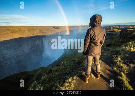 Una giovane donna che guarda la cascata Dettifoss, Islanda. La più grande cascata della comunità europea Foto Stock